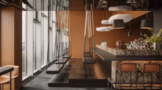 En moderne, stilig bar med et slankt, reflekterende tak og jordfarger. Swing seter linje den ene siden, mens en marmor bar er på den andre, utsmykket med flasker og glass. Store vindusflater gir utsikt utenfor, og dempet belysning skaper en koselig atmosfære.