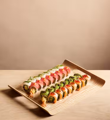 To rader med sushiruller på et rektangulært trefat. Hver rull er toppet med forskjellige ingredienser som fisk, avokado og sauser. Tallerkenen plasseres på en lys treoverflate mot et vanlig bakteppe.